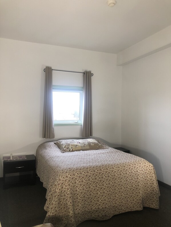 A bedroom with a bed, a window with curtains, a bedside table, and a nightstand.