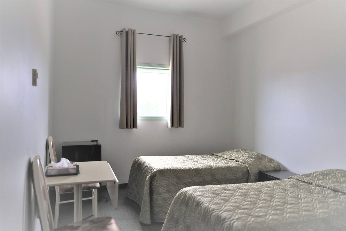 Una habitación con dos camas, un escritorio y una ventana con cortinas.