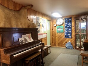A room with a wooden piano, a fur rug, a clock, and a wall with animal illustrations.