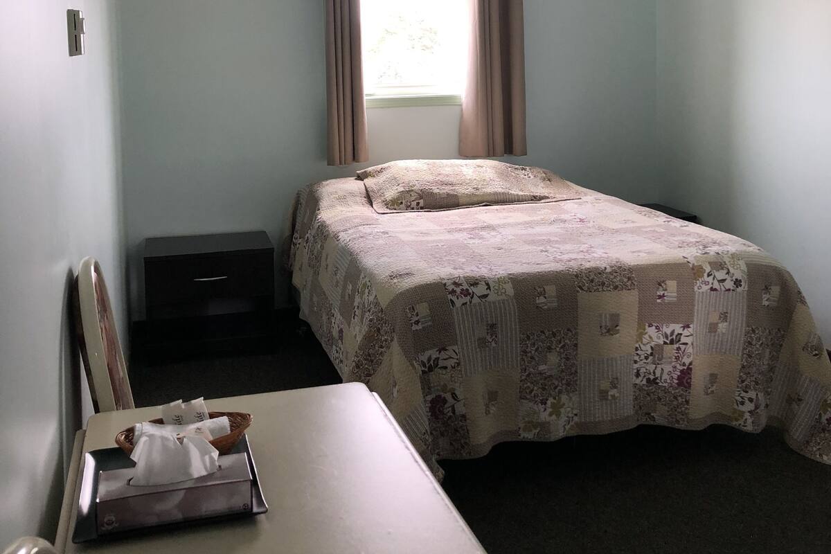 Una habitación pequeña con cama individual, una mesa, una silla, un escritorio y un ventanal con cortinas.