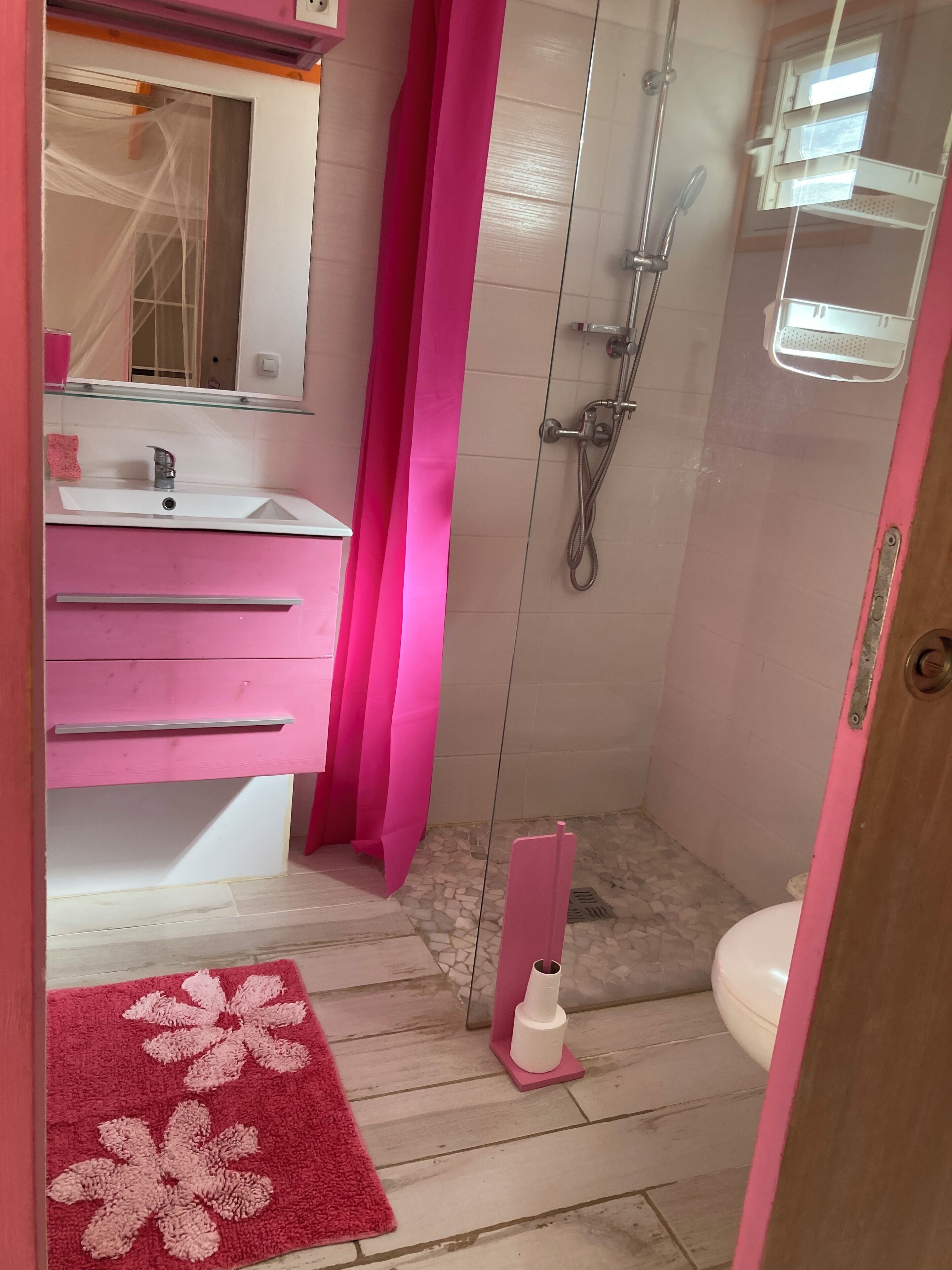 A bathroom with a pink sink, mirror, and shower.