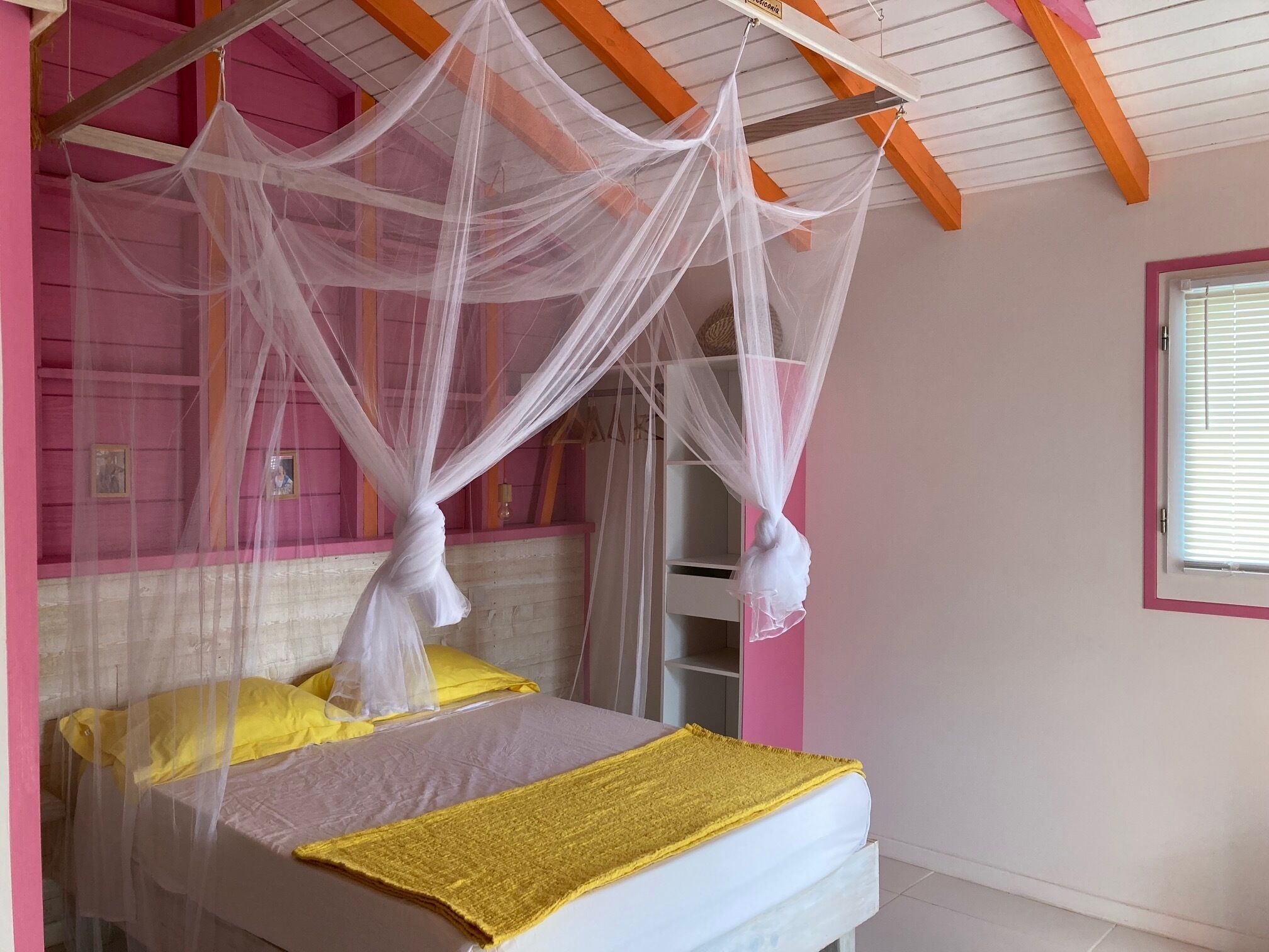 A bed with a canopy, a window with blinds, and a pink wall.