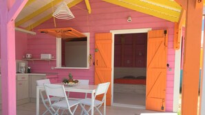 Ein rosafarben-orangefarbenes Zimmer mit Esstisch, Stühlen, einer Küchenzeile und einem Bett.