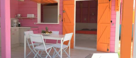 A pink and orange room with a dining table, chairs, a kitchen area, and a bed.