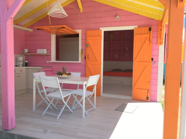 A pink and orange room with a dining table, chairs, a kitchen area, and a bed.