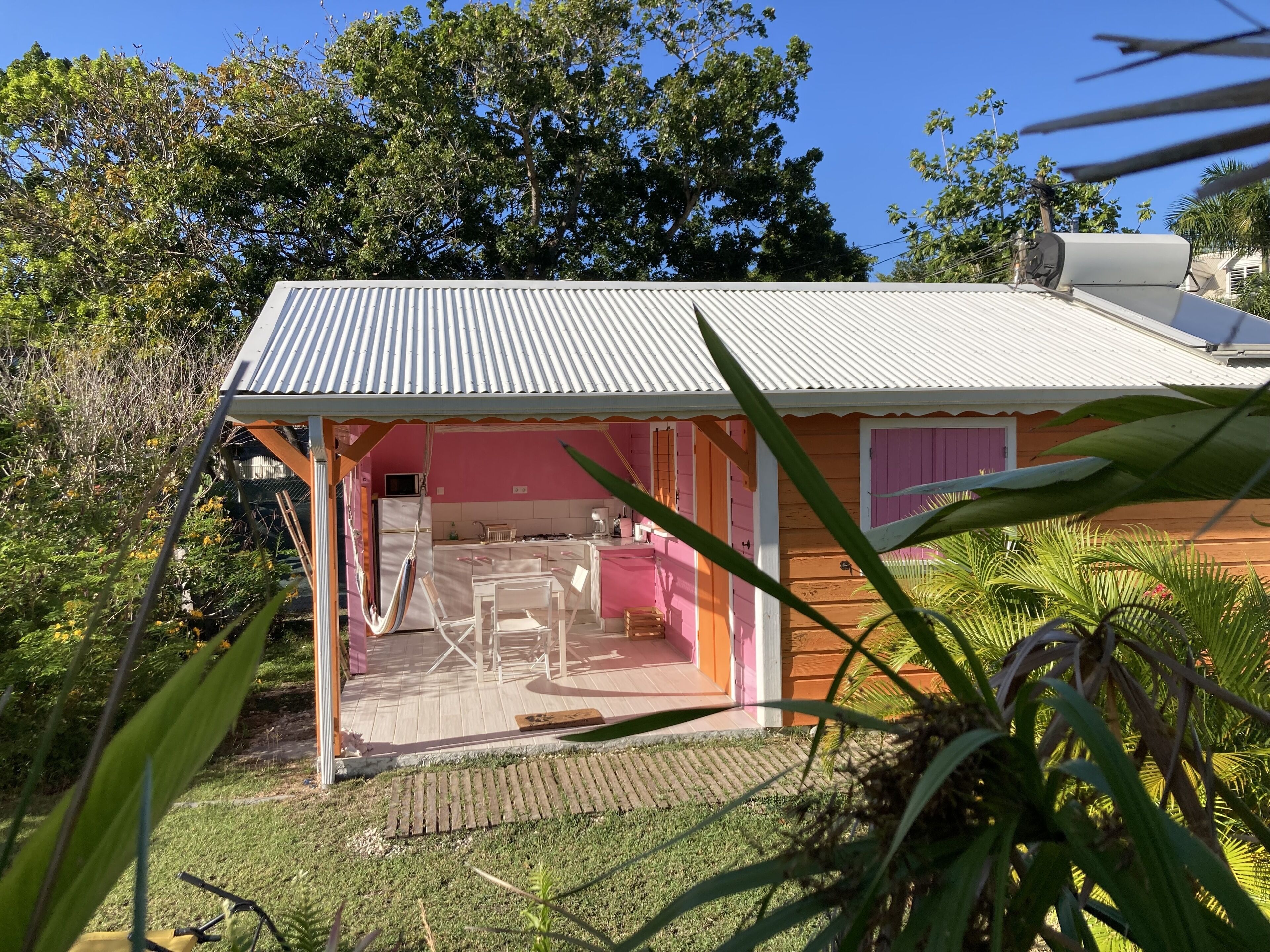 Una pequeña casa con fachada rosa, techo de metal y un patio con mesa y sillas.