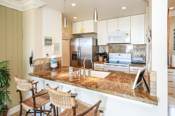 A modern kitchen with granite countertops, stainless steel appliances, and a bar area with wicker chairs.