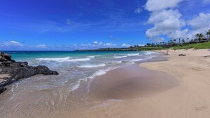 Una playa con aguas azul turquesa, orilla de arena y edificios a lo lejos.