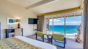 Habitación de hotel con cama, televisión, escritorio, silla, una mesita y vistas al océano.