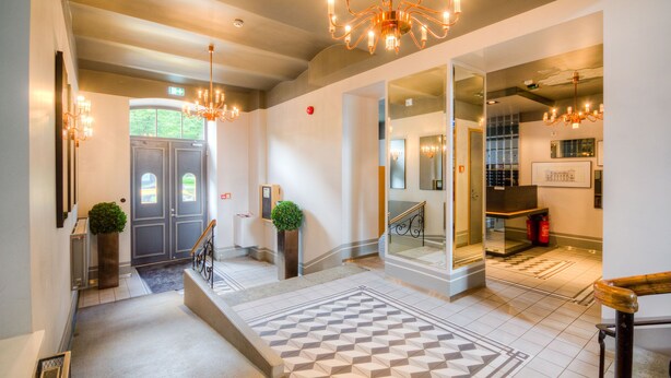 A hotel lobby with a checkered floor, a staircase, and a chandelier.