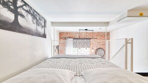 A bedroom with a bed, a brick wall, and a window with a view of the outdoors.