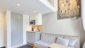 A modern living room with a grey sofa, a wooden coffee table, and a kitchen area with a microwave.