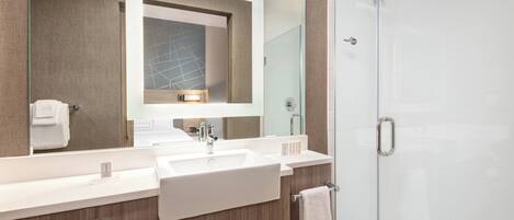 A modern bathroom with a large mirror, two sinks, a glass shower enclosure, and wooden cabinetry.
