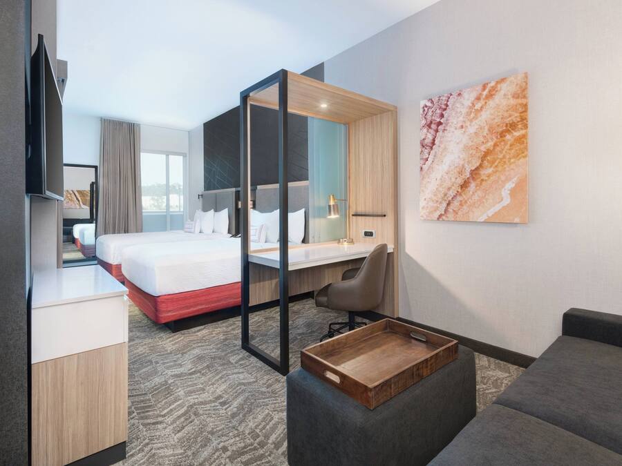 Quarto de hotel moderno com cama, escrivaninha, sofá e televisão.