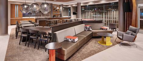 A modern lobby with a seating area, a bar, and a kitchen in the background.