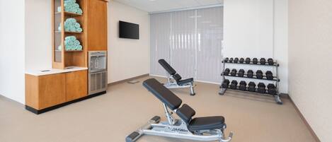 A gym with exercise benches, a water dispenser, and a rack of dumbbells.