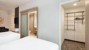 A hotel room with two beds, a wardrobe, a television, and a walk-in closet with hanging clothes.
