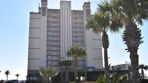 Een meerlaags hotel met een opvallend middelpunt, omringd door palmbomen en een parkeerplaats.