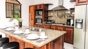A modern kitchen with granite countertops, wooden cabinets, a stainless steel sink, and a built-in oven. - Ocean View Single Story House with Private Infinity Pool.  10 min walk to Beach (Playas del Coco)