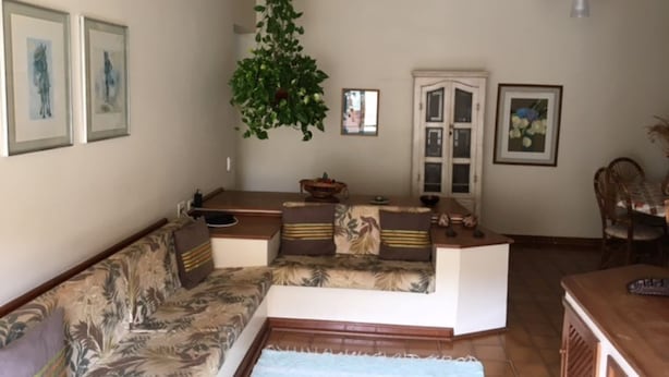 A living room with a sofa, a coffee table, a dining table, and a hanging plant. - Cozy, well-furnished apartment on a quiet street near the beach. (Guaruja)