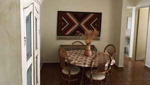 A dining area with a table set for four, surrounded by wicker chairs, a decorative vase, and a large geometric wall hanging. - Cozy, well-furnished apartment on a quiet street near the beach. (Guaruja)