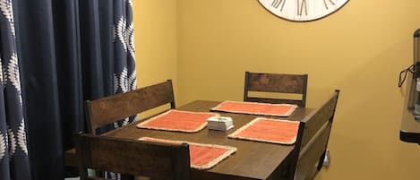 Un comedor con una mesa de madera, cuatro sillas y un reloj de pared grande.