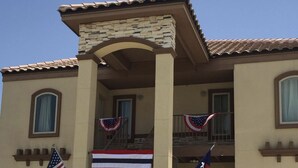 Een gebouw met een stenen gevel, meerdere ramen en een balkon. Amerikaanse en Texas vlaggen zijn uitgestald.