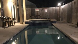 Een zwembad met een hottub in het midden, omgeven door een houten omheining en een paar stoelen.