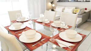 A dining area with a glass table set for four, surrounded by white chairs.
