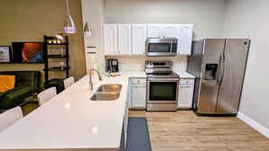 A modern kitchen with white cabinets, stainless steel appliances, a built-in oven, and a large island with a sink.