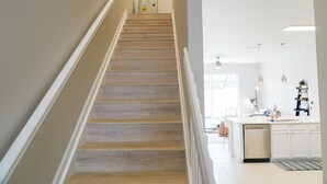 A staircase with wooden steps leading to a kitchen area with white cabinets and a central island.