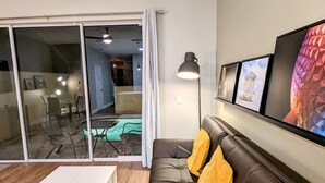A modern living room with a leather sofa, a white coffee table, and a large sliding glass door leading to a pool area.