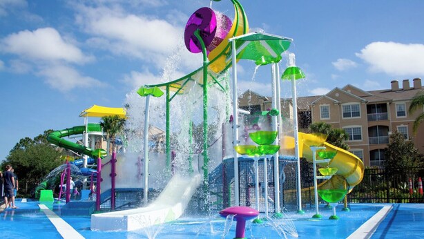 A water park with multiple slides and water features, surrounded by a pool and a building in the background.