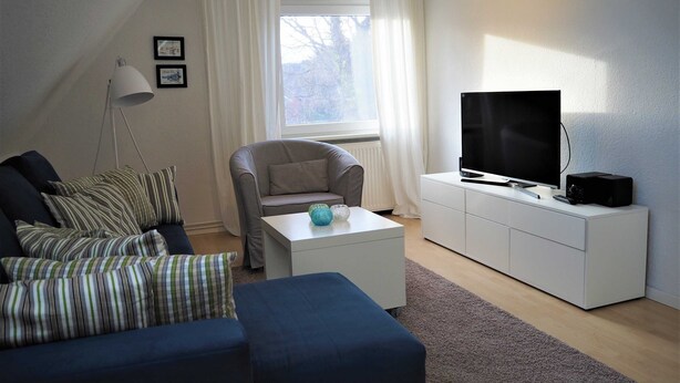 Ein modernes Wohnzimmer mit einer Couch, einem Sessel und einem Fernseher auf einem weißen Schrank.