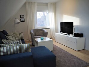 En moderne stue med sofa, lænestol og et fjernsyn på et hvidt skab.