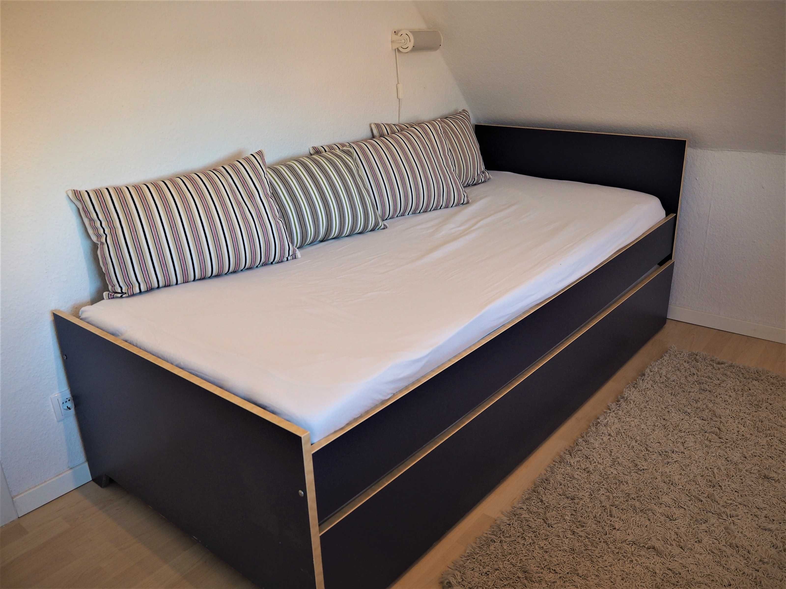 A single bed with a dark frame and a light-colored mattress, accompanied by striped pillows.