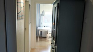 Ein schmaler Flur mit einem weißen Tisch, Stühlen, einem blauen Kühlschrank und einer Heizung.
