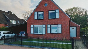 Ein zweistöckiges, rotes Backsteinhaus mit einem Giebeldach, einer Garage und einem schwarzen Metallzaun.