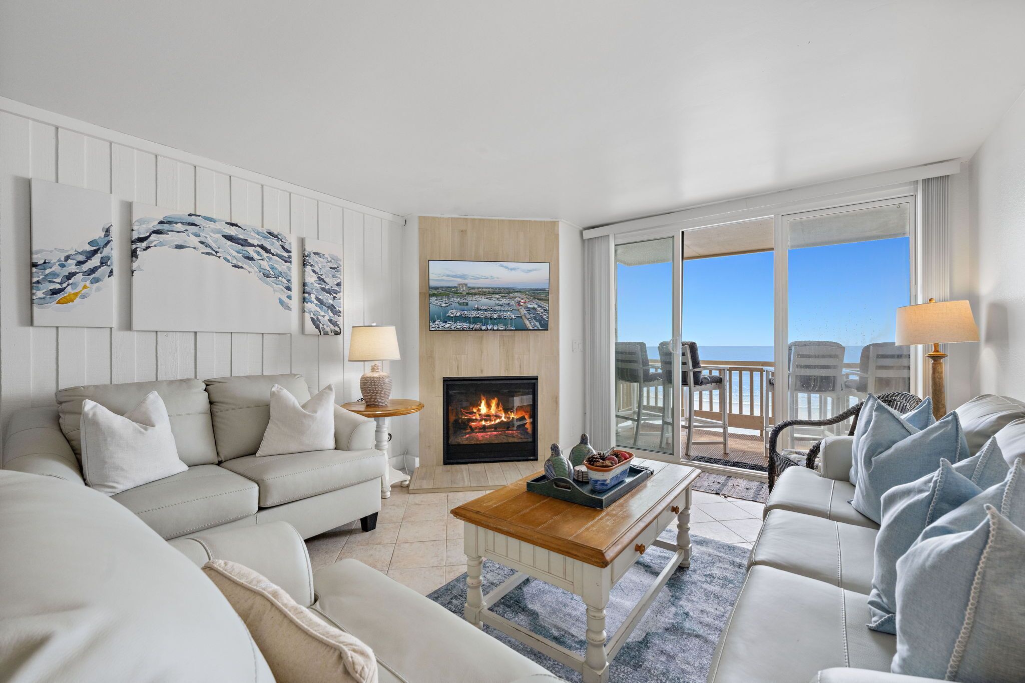 A living room with a fireplace, a sofa set, a coffee table, and a view of the ocean through large windows.