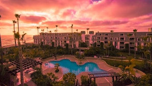 Ein Resort mit Pool, Palmen und Blick auf den Ozean bei Sonnenuntergang.