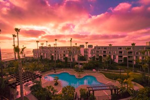 A resort with a pool, palm trees, and a view of the ocean at sunset.