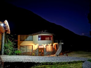 Un edificio de dos pisos con fachada de piedra, una puerta roja y una escalera que lleva al piso superior.