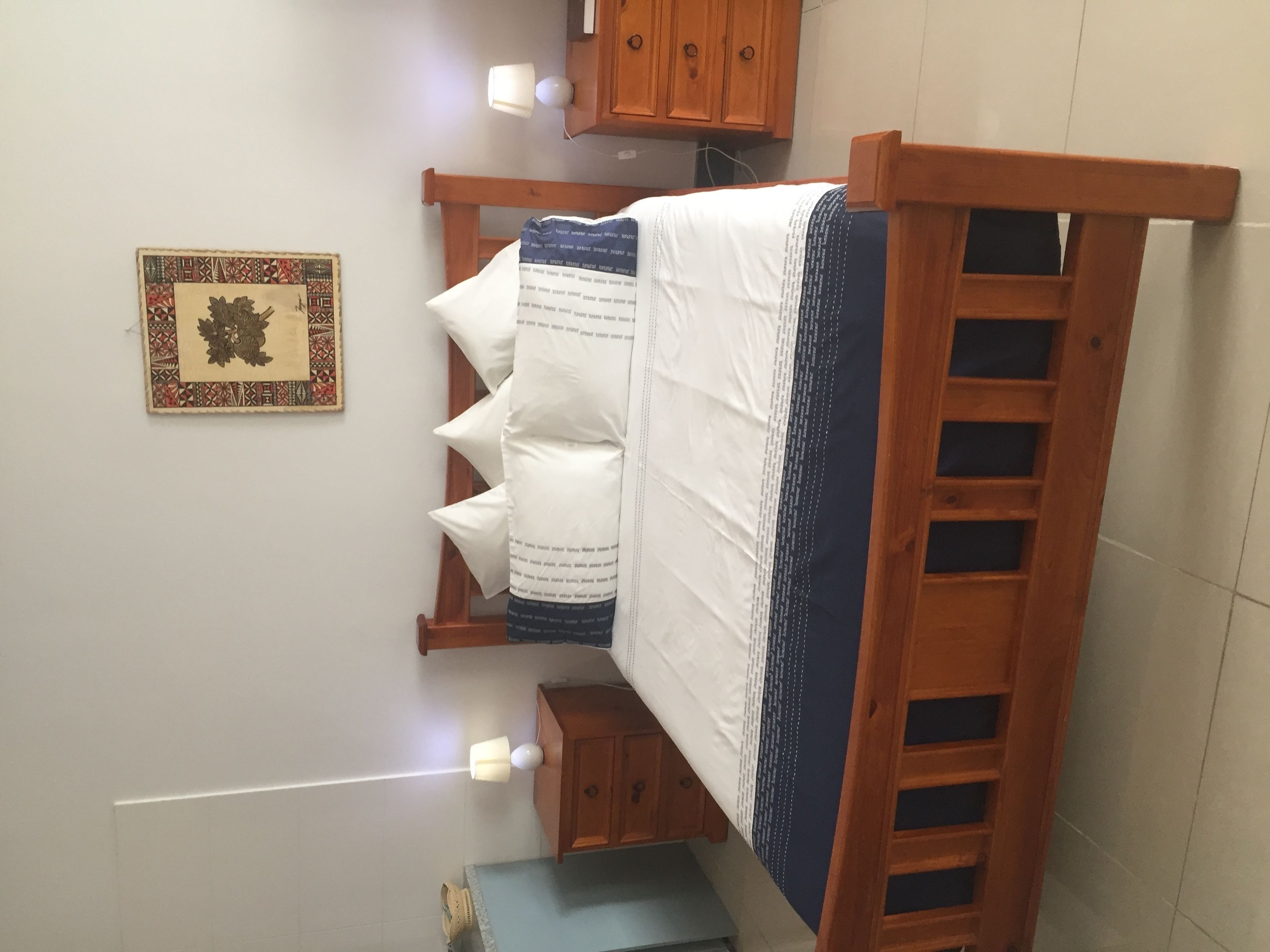 A small, compact room with a wooden bed, a small cabinet, and a framed picture on the wall.