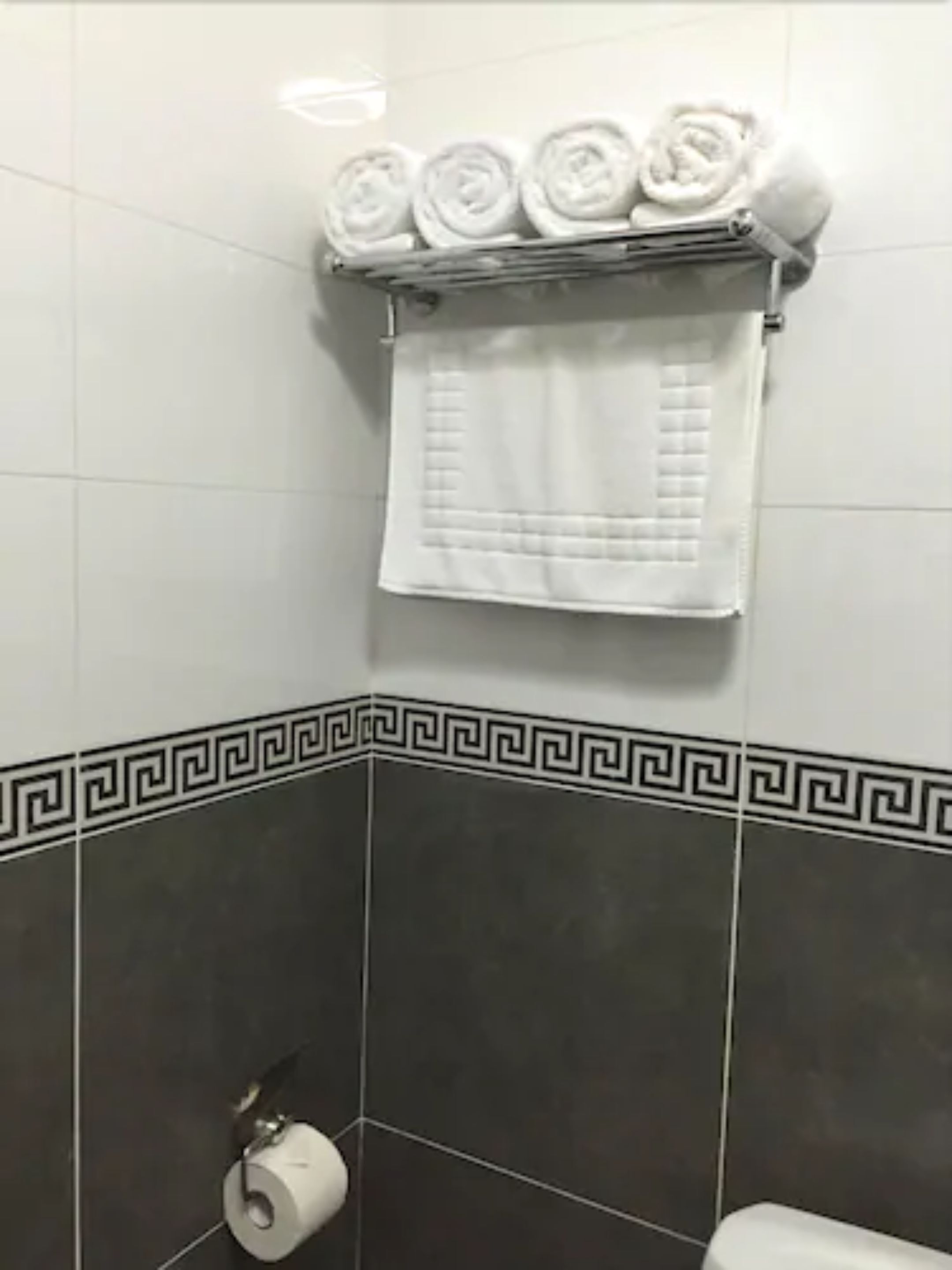 A bathroom with dark tiles, a white towel rack with folded towels, and a toilet paper holder.