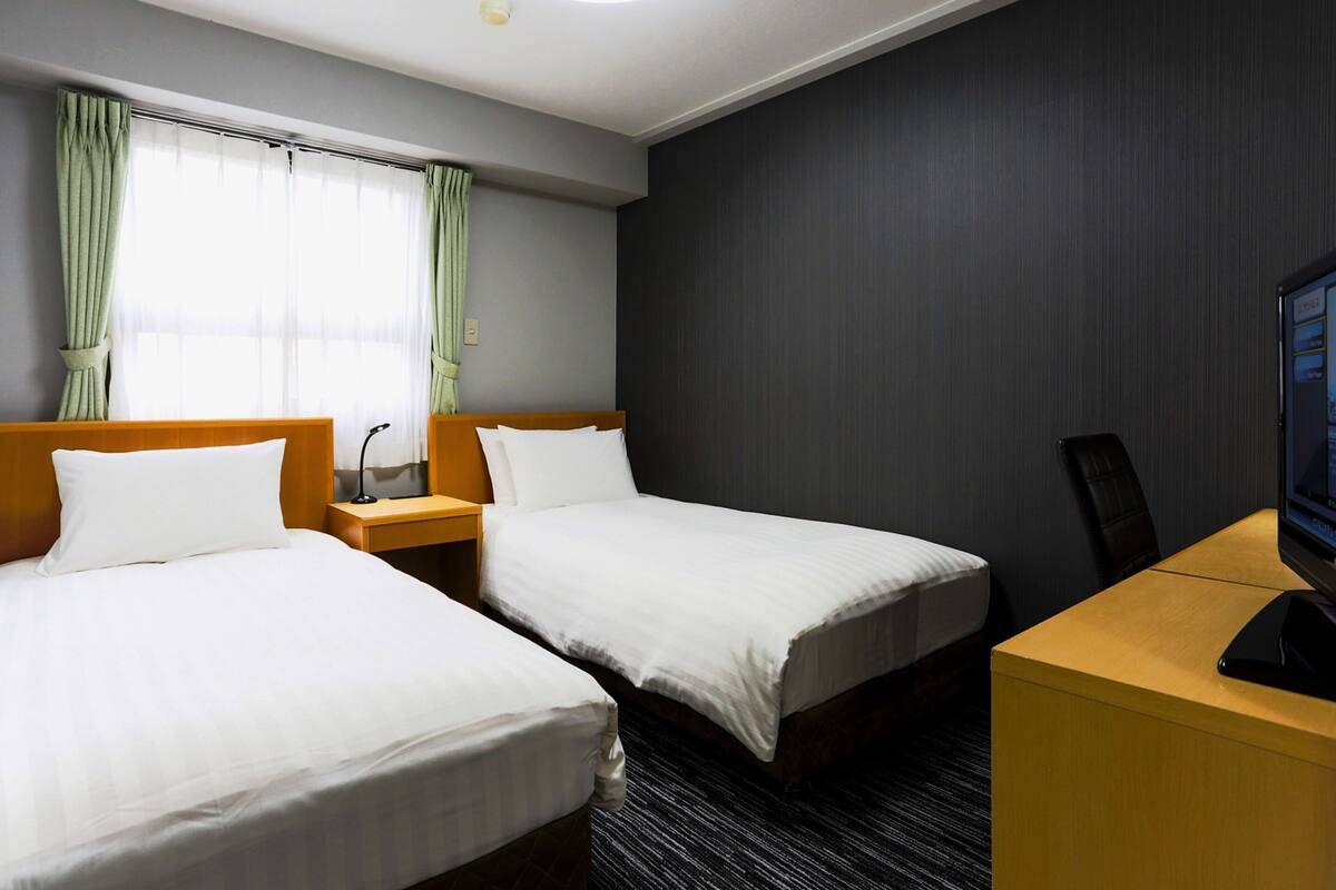 A hotel room with two beds, a desk, and a television.