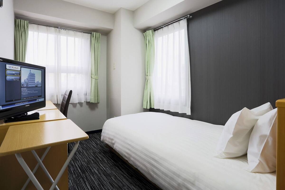 A hotel room with a bed, a desk, and a television displaying a cityscape.
