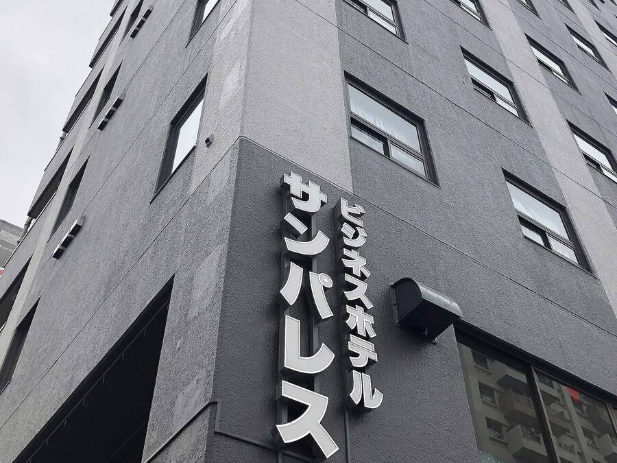 Um edifício alto com design arquitetônico moderno, com várias janelas e uma placa bem visível com caracteres japoneses.