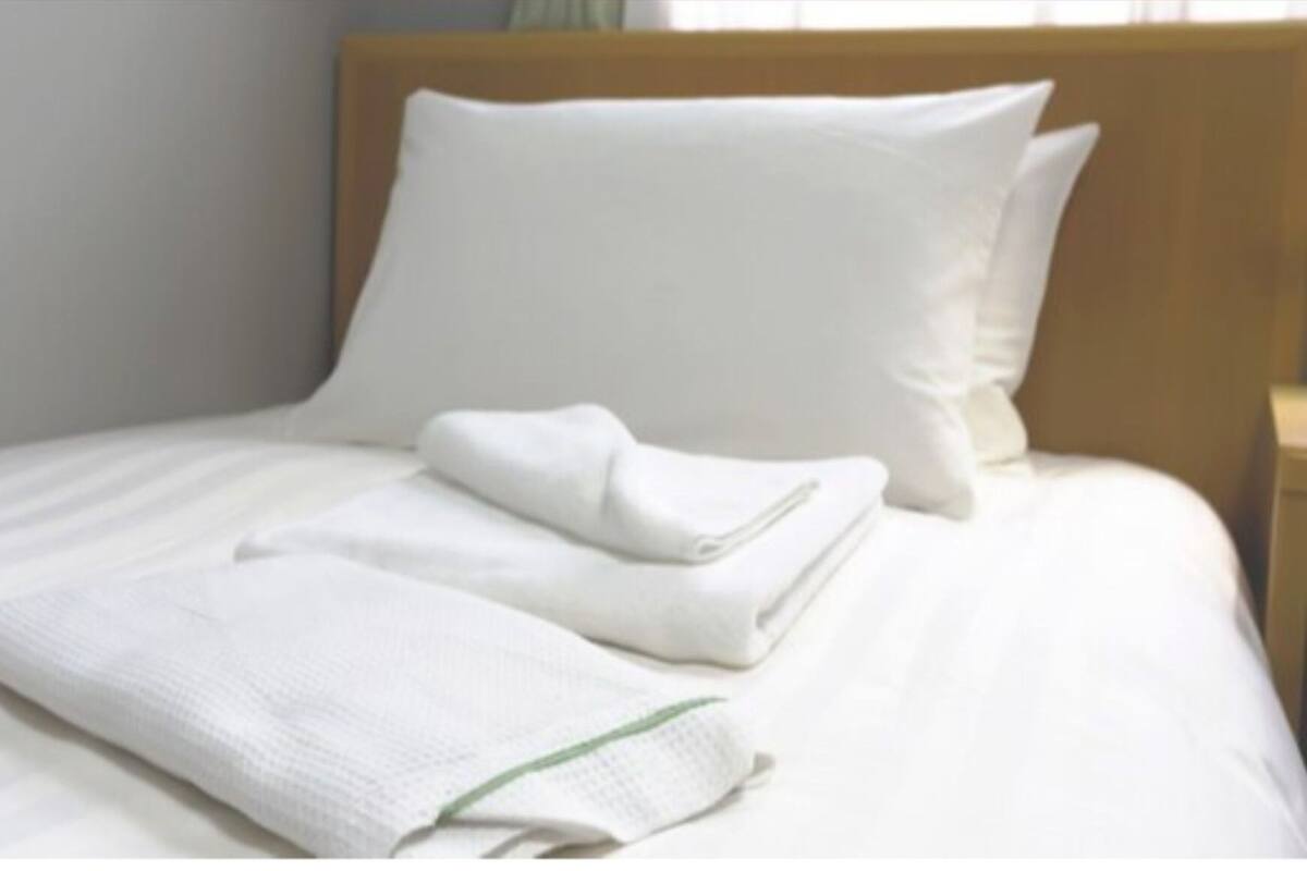 A neatly made bed with white linens and pillows, a folded towel, and a wooden headboard.