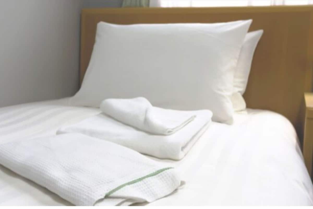 A neatly made bed with white linens and pillows, a folded towel, and a wooden headboard.