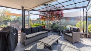 A covered patio area with a sofa, two armchairs, a table, and a barbecue grill.